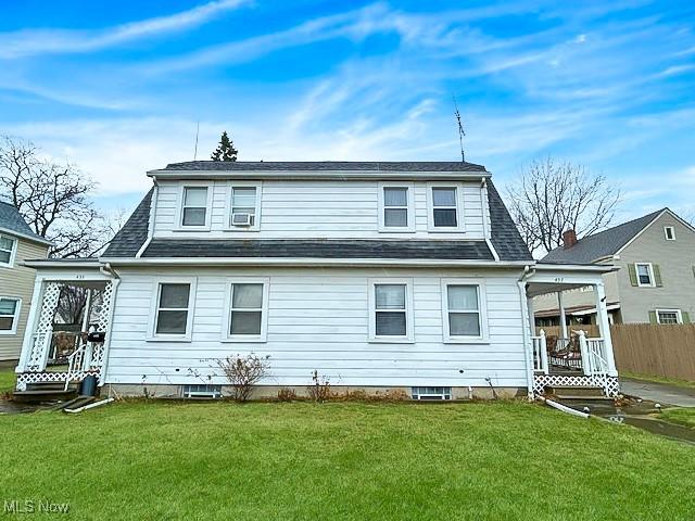 back of house with a shingled roof, a lawn, and fence