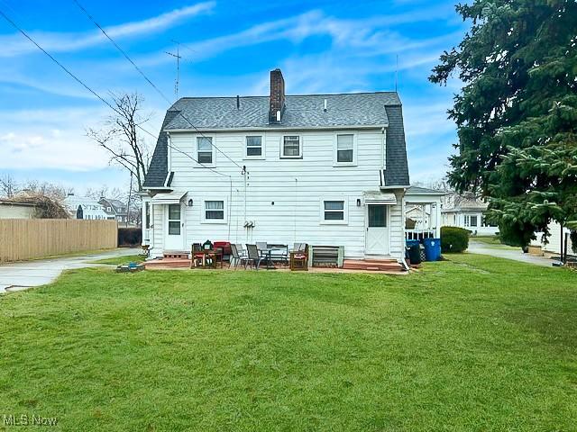 back of house with a yard, fence, a chimney, and a shingled roof