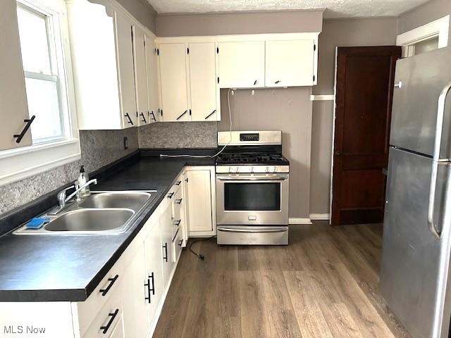 kitchen with appliances with stainless steel finishes, dark wood-style flooring, dark countertops, and a sink