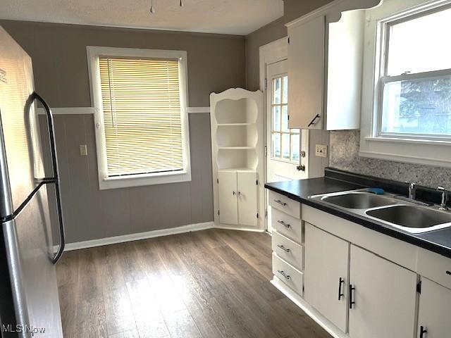 kitchen with a sink, white cabinets, a wealth of natural light, freestanding refrigerator, and dark countertops