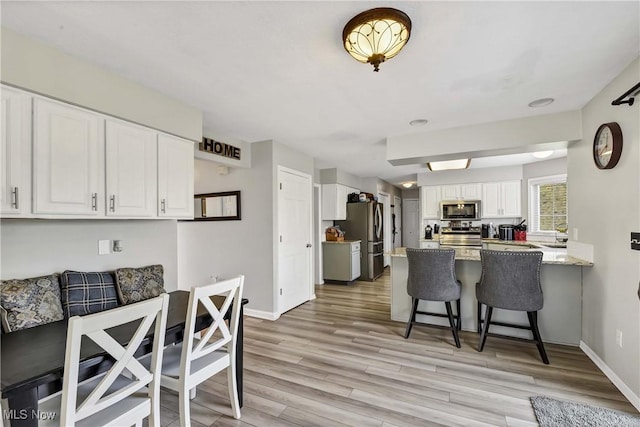 kitchen with white cabinetry, stainless steel appliances, light stone countertops, a kitchen bar, and kitchen peninsula