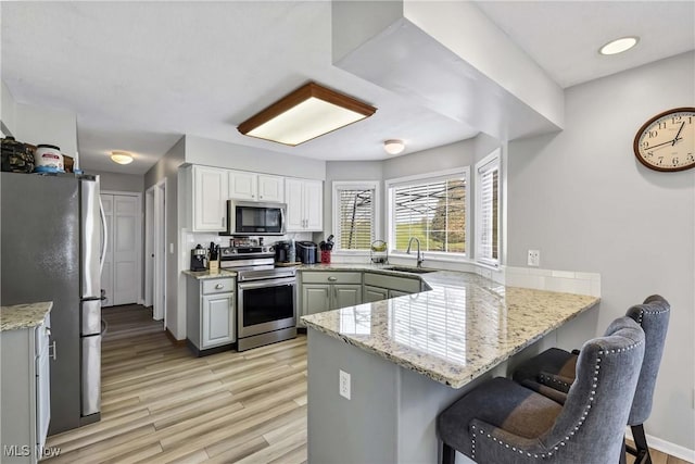 kitchen with sink, a breakfast bar, appliances with stainless steel finishes, light stone counters, and kitchen peninsula