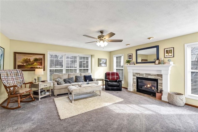 carpeted living room with ceiling fan, a stone fireplace, plenty of natural light, and a textured ceiling