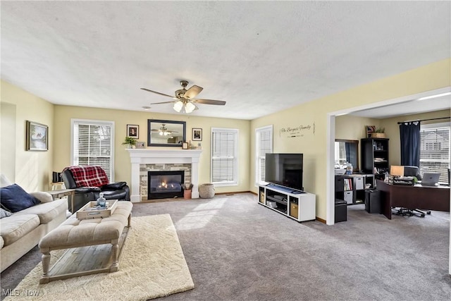 living room with ceiling fan, a stone fireplace, carpet flooring, and a textured ceiling