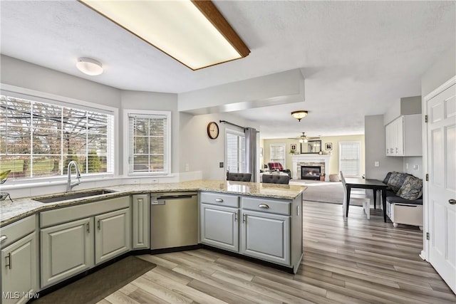 kitchen with a stone fireplace, sink, stainless steel dishwasher, kitchen peninsula, and light hardwood / wood-style flooring