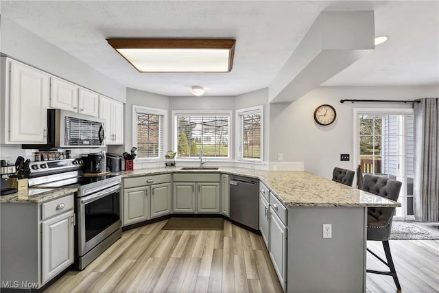 kitchen featuring a breakfast bar, sink, light stone counters, kitchen peninsula, and stainless steel appliances