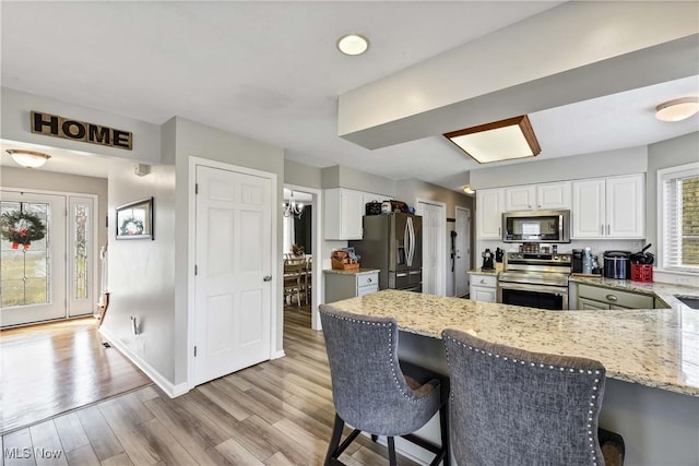 kitchen featuring light hardwood / wood-style flooring, white cabinetry, a kitchen breakfast bar, stainless steel appliances, and kitchen peninsula