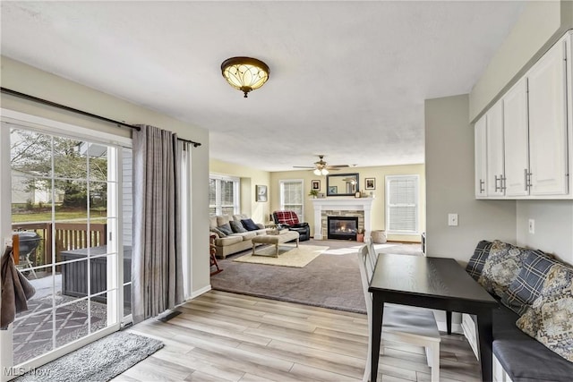 living room with a stone fireplace, light hardwood / wood-style flooring, and ceiling fan