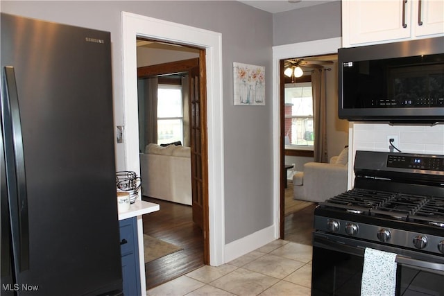 kitchen featuring stainless steel gas range, refrigerator, white cabinetry, backsplash, and light tile patterned flooring