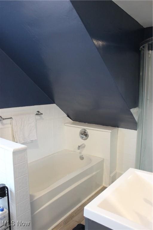 bathroom featuring vaulted ceiling, wood-type flooring, sink, and a bathtub