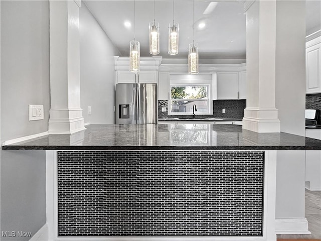 kitchen featuring stainless steel fridge, decorative columns, hanging light fixtures, and white cabinets