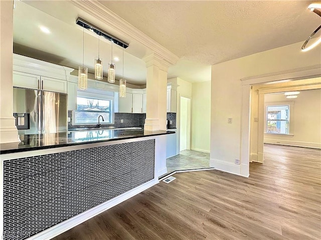 kitchen with decorative columns, white cabinetry, stainless steel fridge, hanging light fixtures, and light hardwood / wood-style floors