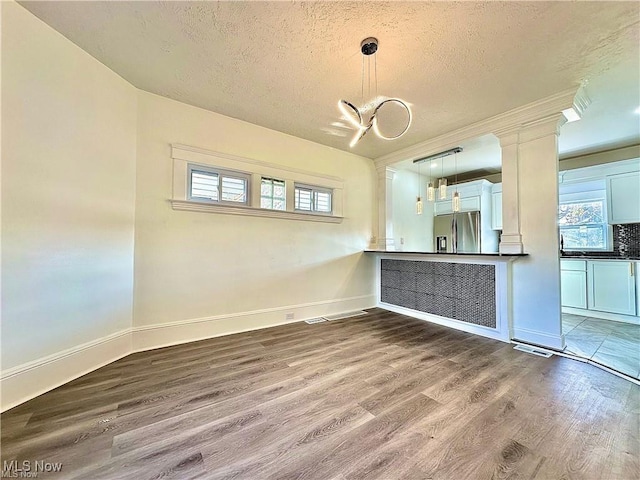 interior space featuring a textured ceiling, stainless steel fridge, pendant lighting, hardwood / wood-style floors, and white cabinets