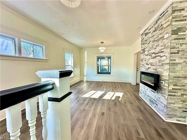 unfurnished living room with hardwood / wood-style flooring, crown molding, a stone fireplace, and a textured ceiling