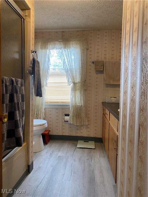 bathroom with a shower with shower door, wood-type flooring, vanity, toilet, and a textured ceiling