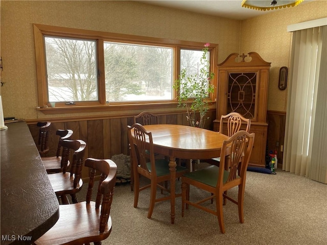 dining area with light carpet, a healthy amount of sunlight, and wood walls