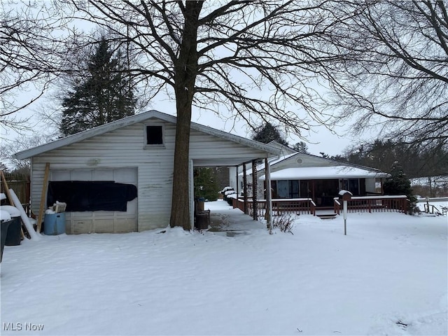 snow covered property with a garage, an outdoor structure, and a porch