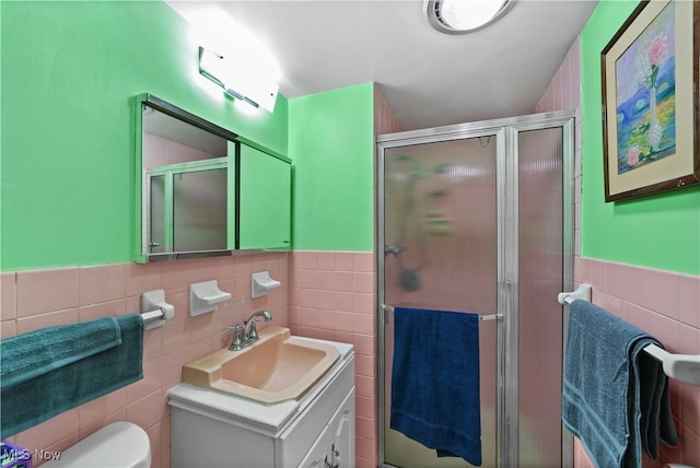 bathroom featuring vanity, toilet, a shower with shower door, and tile walls