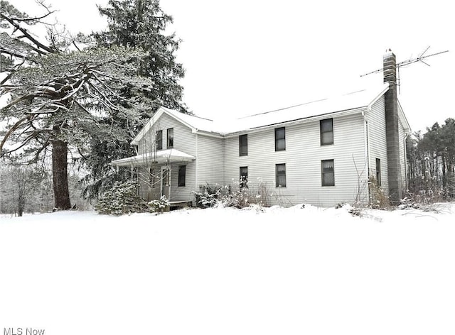 snow covered facade featuring a chimney