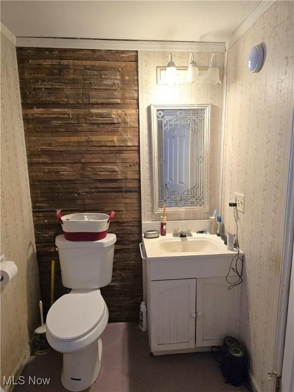 half bath featuring toilet, vanity, and wallpapered walls