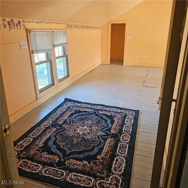 unfurnished room featuring baseboards, lofted ceiling, and wood finished floors