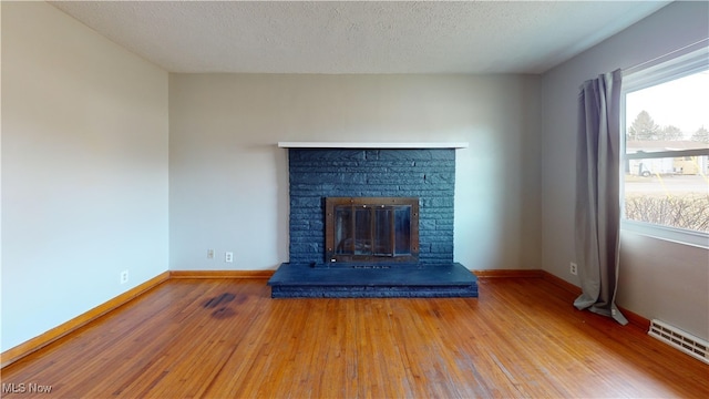 unfurnished living room with hardwood / wood-style floors, a stone fireplace, and a textured ceiling