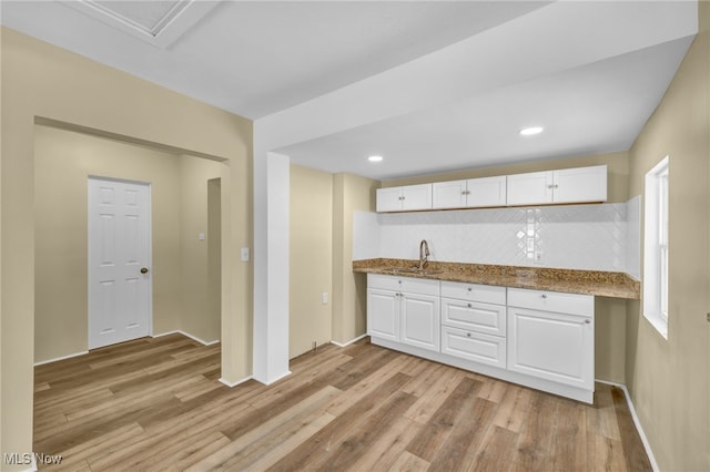 kitchen with sink, light hardwood / wood-style flooring, white cabinets, and stone countertops