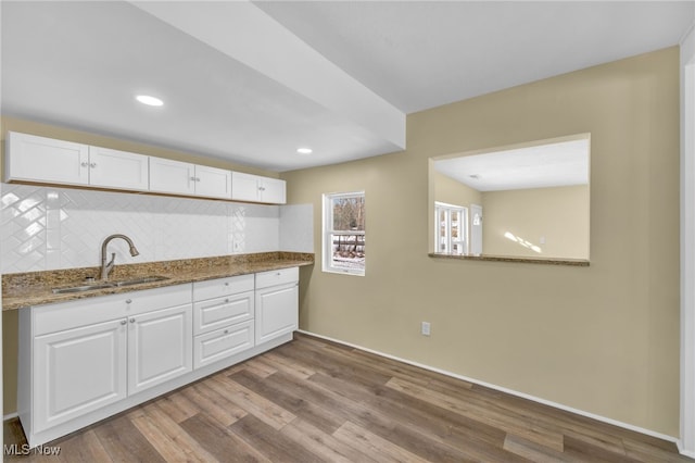 kitchen with stone countertops, sink, white cabinets, backsplash, and light hardwood / wood-style floors