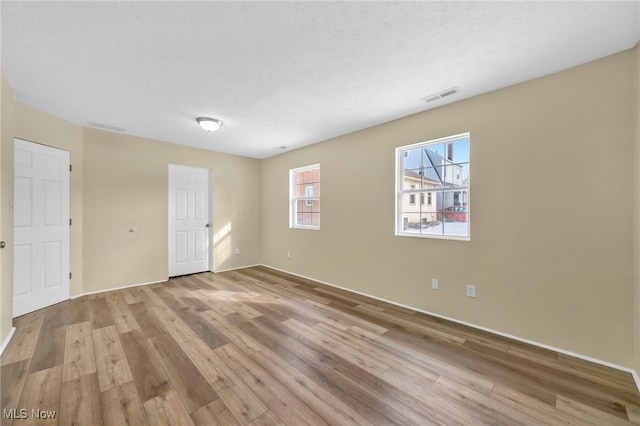 spare room with a textured ceiling and light hardwood / wood-style flooring