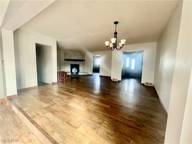 unfurnished living room featuring dark hardwood / wood-style flooring, a stone fireplace, and a notable chandelier