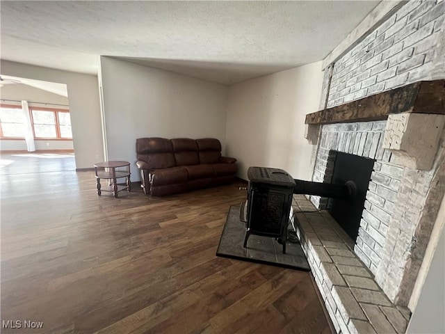 living room with ceiling fan, a brick fireplace, dark wood-type flooring, and a textured ceiling