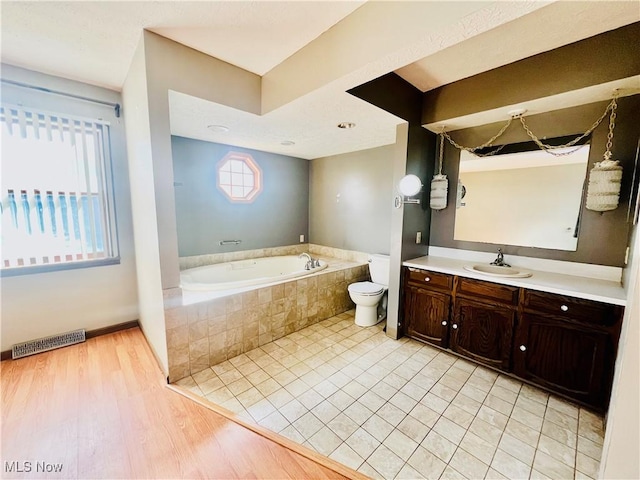 bathroom featuring tiled tub, vanity, a wealth of natural light, and toilet