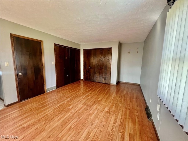 unfurnished bedroom with multiple closets, a textured ceiling, and light wood-type flooring