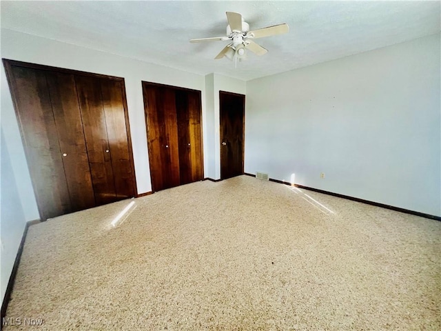 unfurnished bedroom featuring ceiling fan and two closets