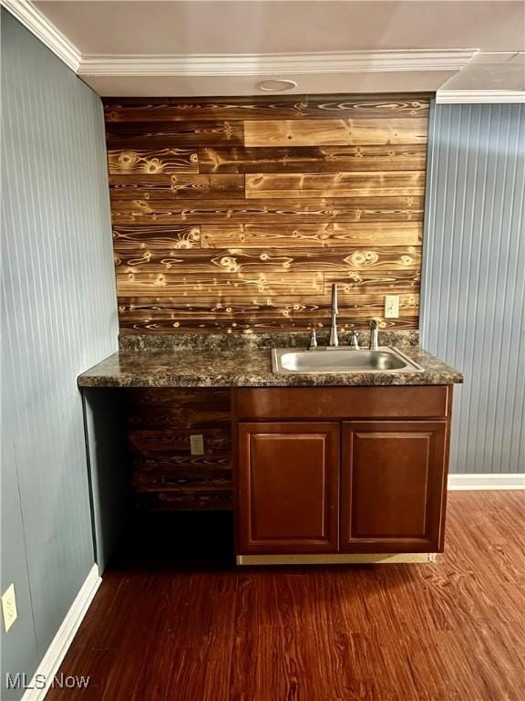 bar with sink, dark wood-type flooring, ornamental molding, and dark stone counters