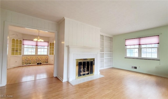 unfurnished living room featuring built in shelves, crown molding, light hardwood / wood-style floors, and a notable chandelier