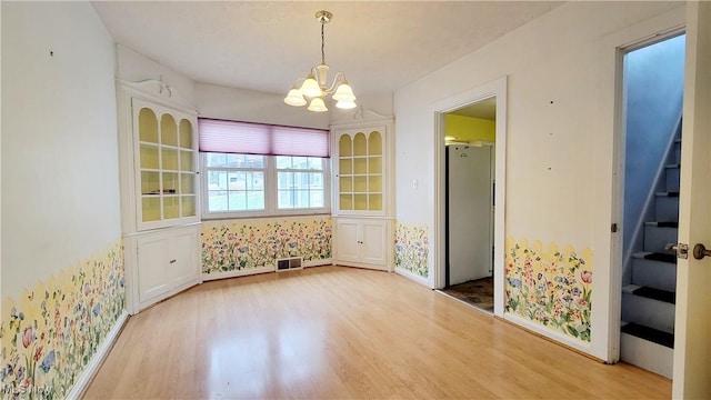 unfurnished dining area featuring an inviting chandelier and hardwood / wood-style floors