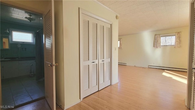 corridor with baseboard heating, a healthy amount of sunlight, and light wood-type flooring