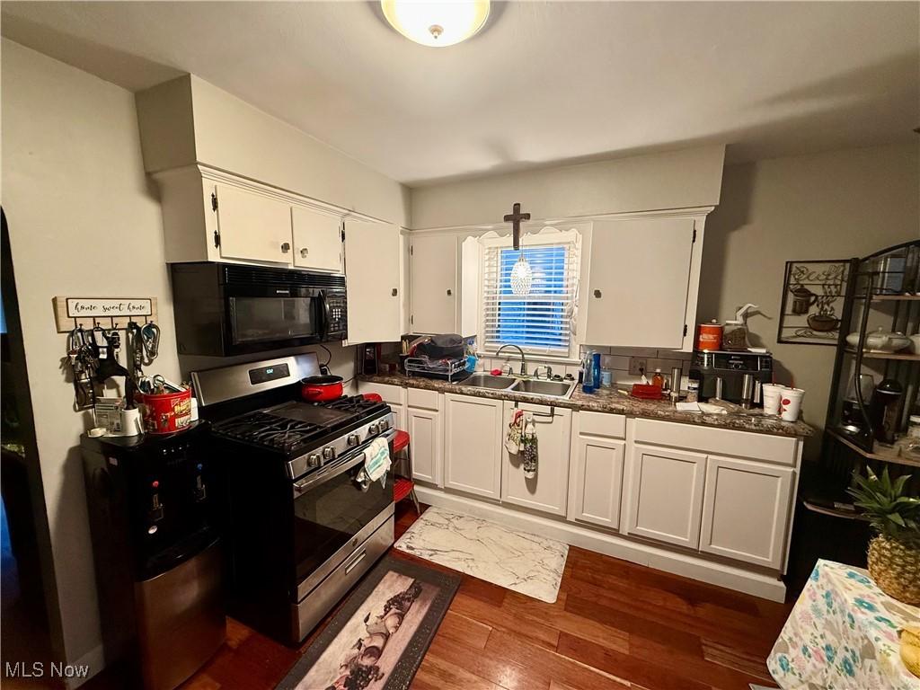 kitchen with stainless steel gas stove, sink, white cabinets, dark hardwood / wood-style flooring, and hanging light fixtures