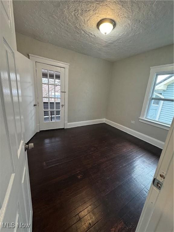 empty room with dark hardwood / wood-style flooring, a textured ceiling, and a wealth of natural light