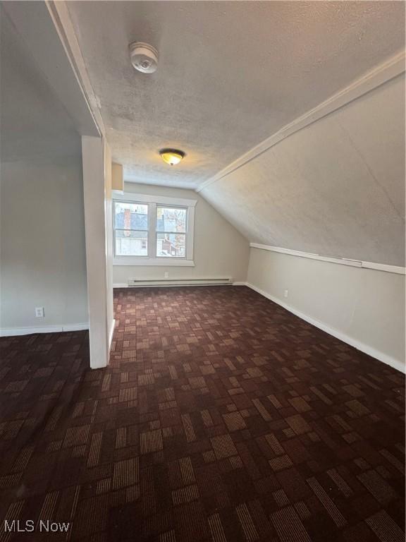 additional living space with a baseboard radiator, lofted ceiling, and a textured ceiling