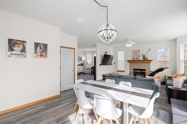 dining space with dark hardwood / wood-style floors, a tiled fireplace, and ceiling fan with notable chandelier