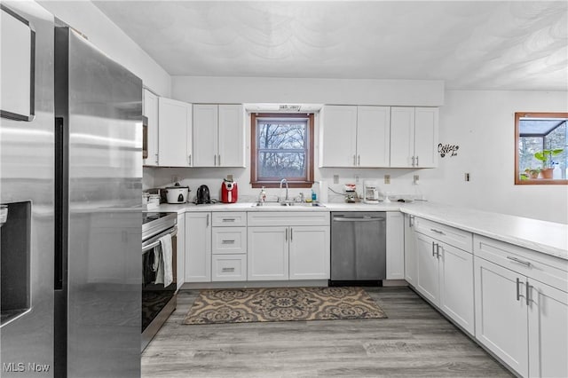 kitchen with stainless steel appliances, sink, white cabinets, and light hardwood / wood-style flooring