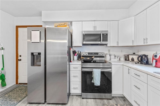 kitchen featuring appliances with stainless steel finishes, light stone countertops, light hardwood / wood-style floors, and white cabinets