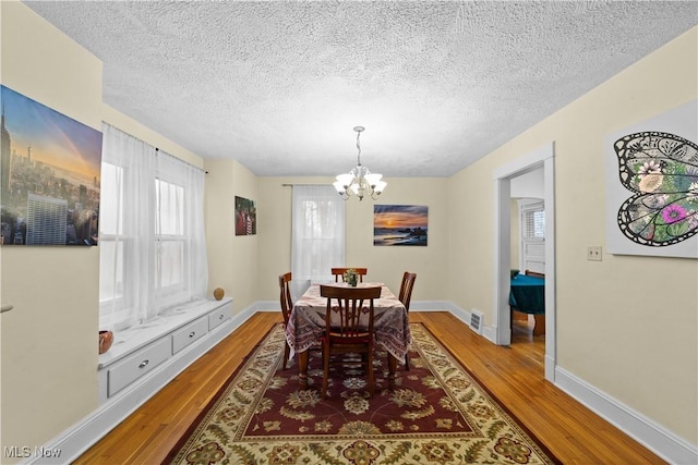 dining space with hardwood / wood-style floors, a textured ceiling, and a notable chandelier