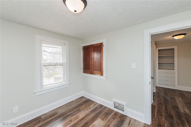 unfurnished room with a textured ceiling and dark hardwood / wood-style flooring