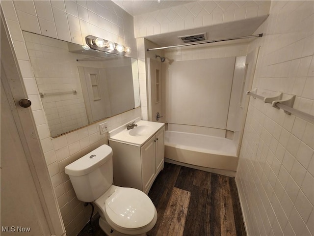 full bathroom with hardwood / wood-style floors, tile walls, vanity, toilet, and washtub / shower combination