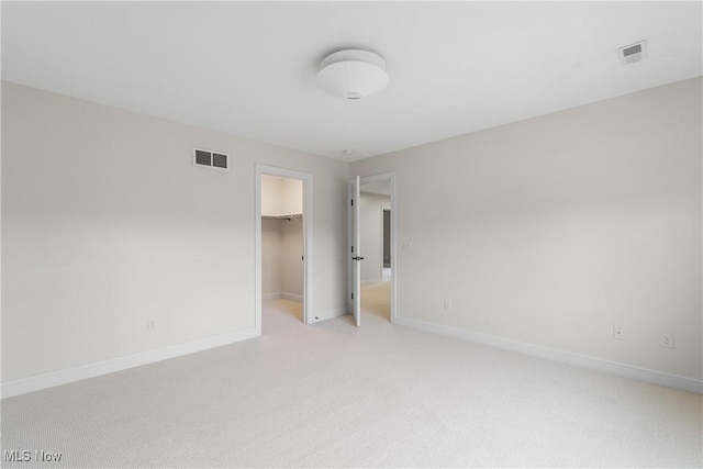 unfurnished bedroom featuring a spacious closet, light colored carpet, and a closet