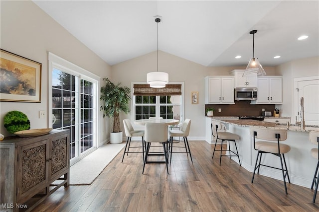 kitchen featuring lofted ceiling, a breakfast bar, white cabinetry, hanging light fixtures, and light stone countertops