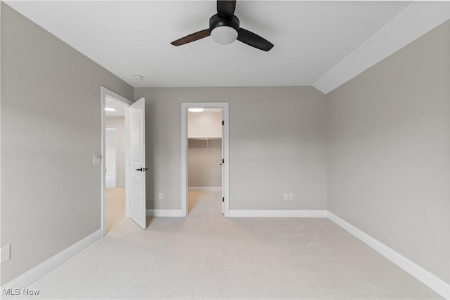 unfurnished bedroom featuring a walk in closet, vaulted ceiling, light carpet, a closet, and ceiling fan